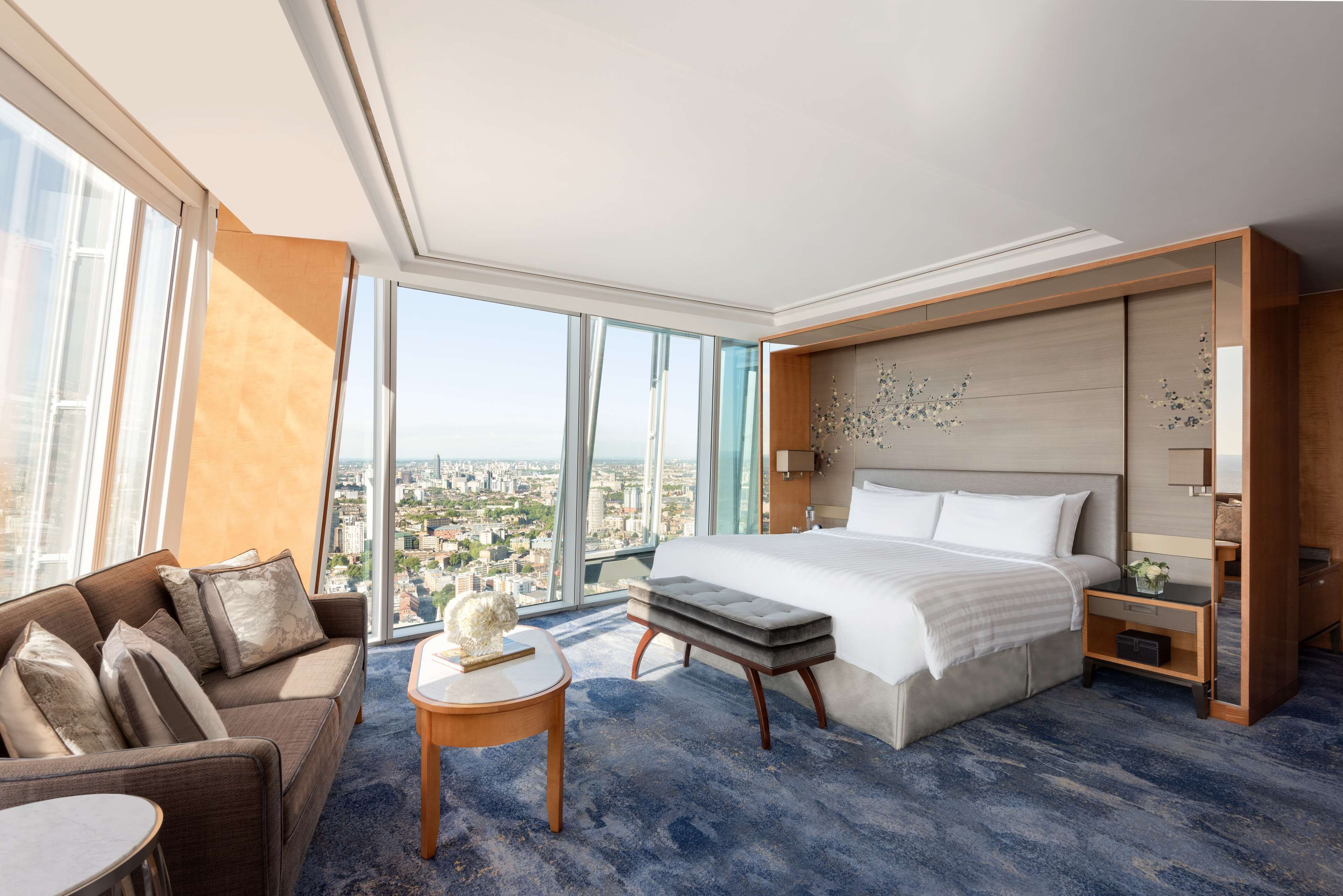 A modern hotel room with a large bed, a sofa, a small table, and a view of the city.