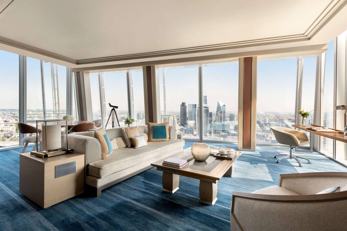 A spacious living room with a large city view, a sofa, a coffee table, and a desk with a chair.