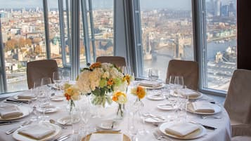 Ein Esstisch, gedeckt für eine Mahlzeit, mit Blick auf die Stadt, großen Fenstern und einer Blumenvase.