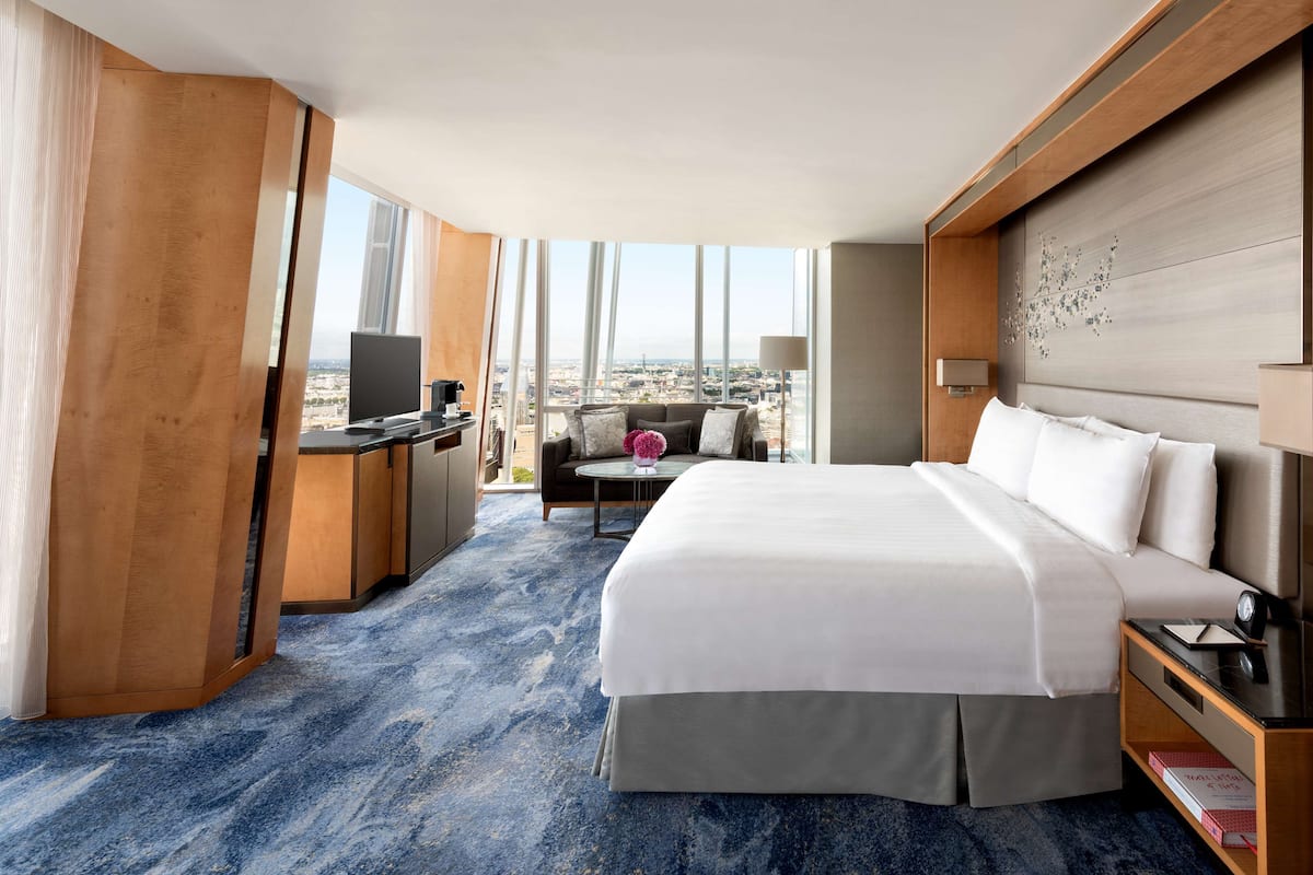 A hotel room with a large bed, a desk, a chair, a TV, and a view of the city.