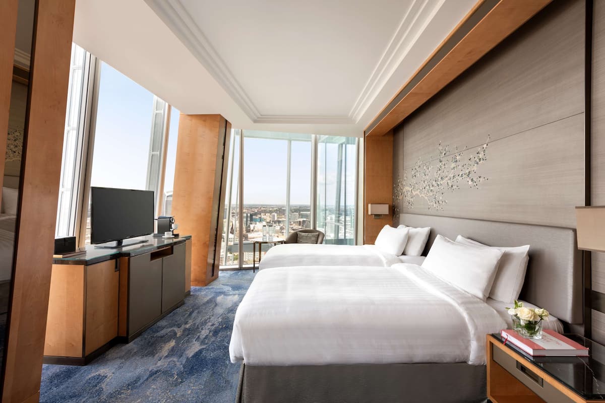 A hotel room with two beds, a desk with a TV, and a city view.