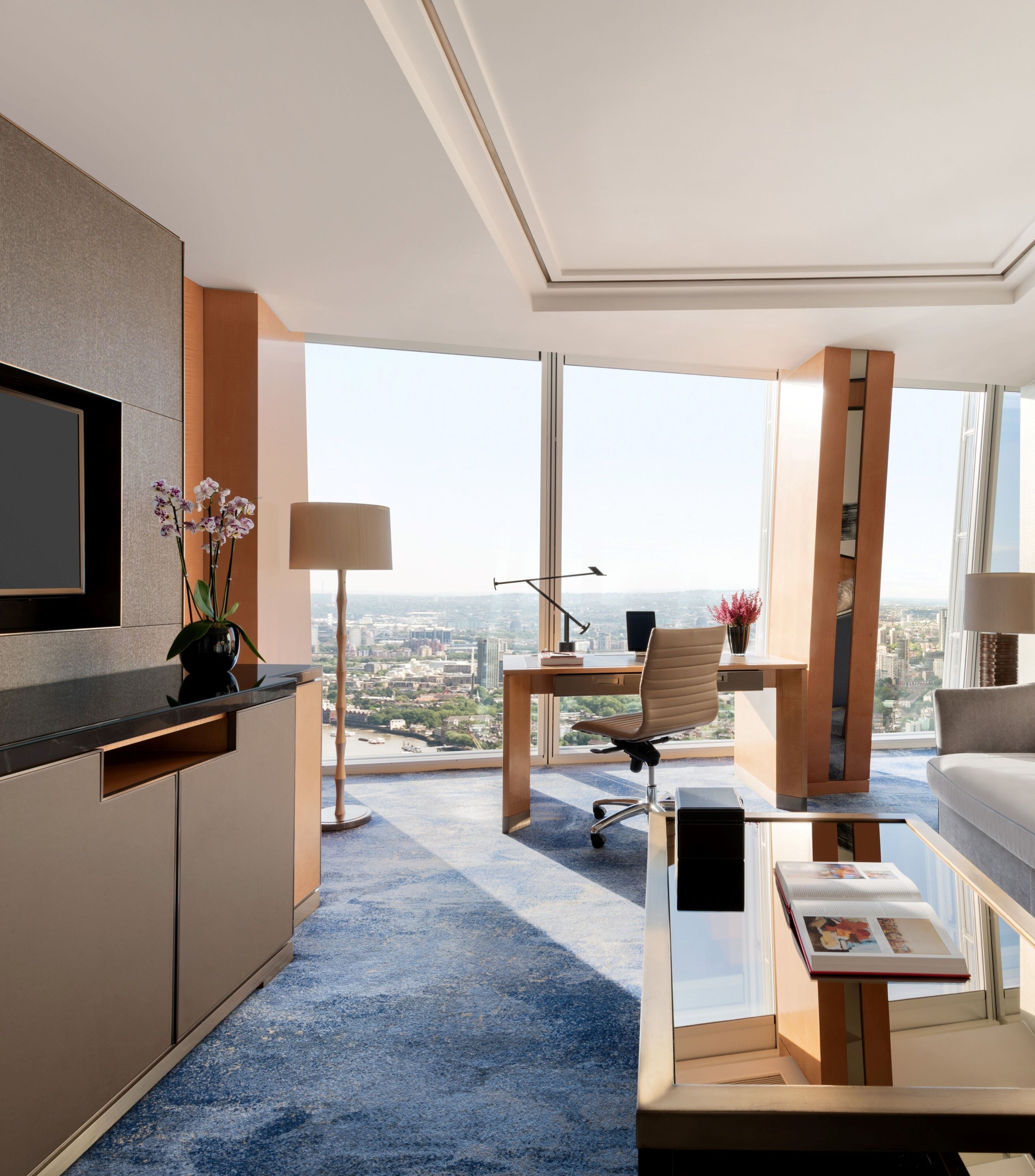 Ein modernes Hotelzimmer mit großem Fenster, Schreibtisch, Sessel, Sofa und Flachbildfernseher.
