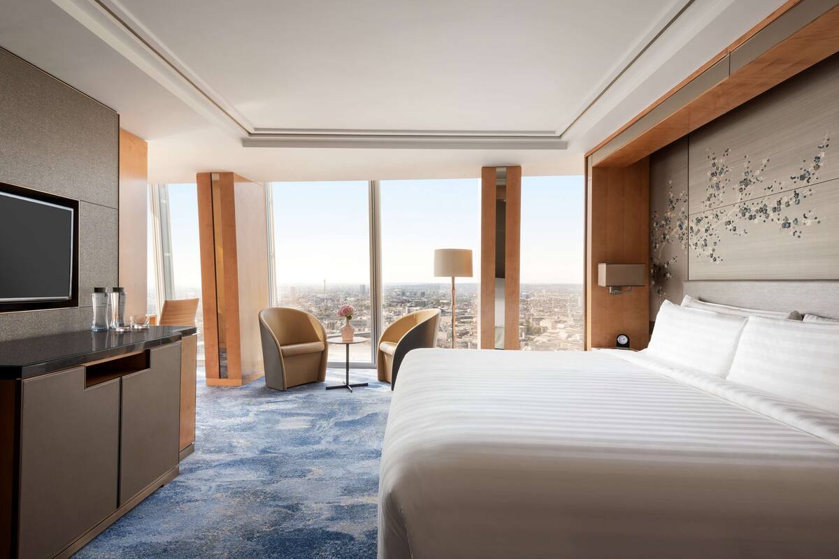 A hotel room with a large bed, a desk with a TV, and a view of the city.