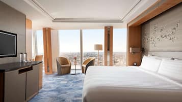 Ein Hotelzimmer mit einem großen Bett, einem Schreibtisch mit Fernseher und Blick auf die Stadt.