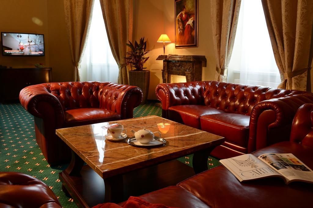 A room with leather sofas, a marble coffee table with tea set, a lamp, and a painting on the wall.