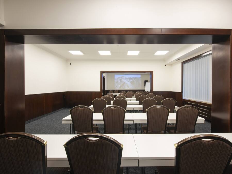 A conference room with a long table and chairs, a projection screen, and a window with blinds.
