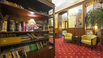 Una biblioteca con estanterías, una lámpara y un área con alfombra roja y dos sillones.