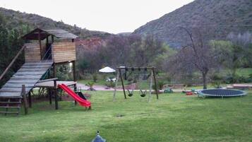 Explore the outdoor play area with a wooden play structure featuring a slide, swings, and trampoline, set amidst a beautifully manicured lawn with scenic views.