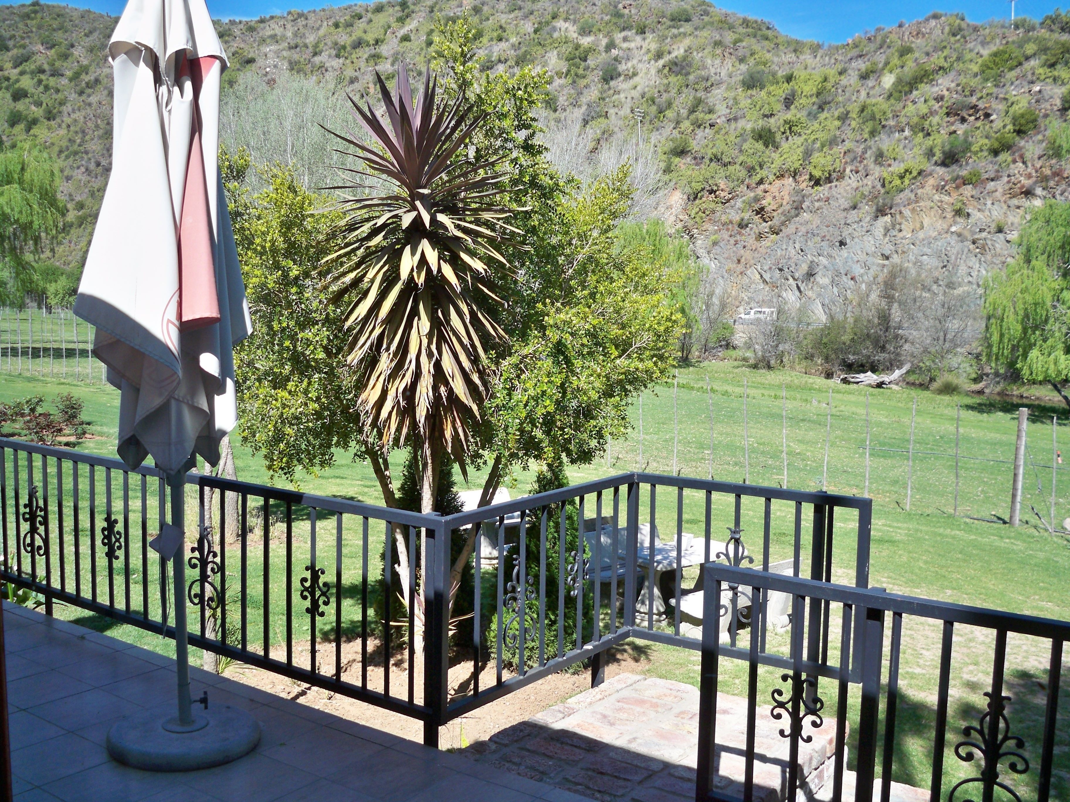 Un balcon avec une balustrade en métal, un pot de fleurs et un parasol blanc.