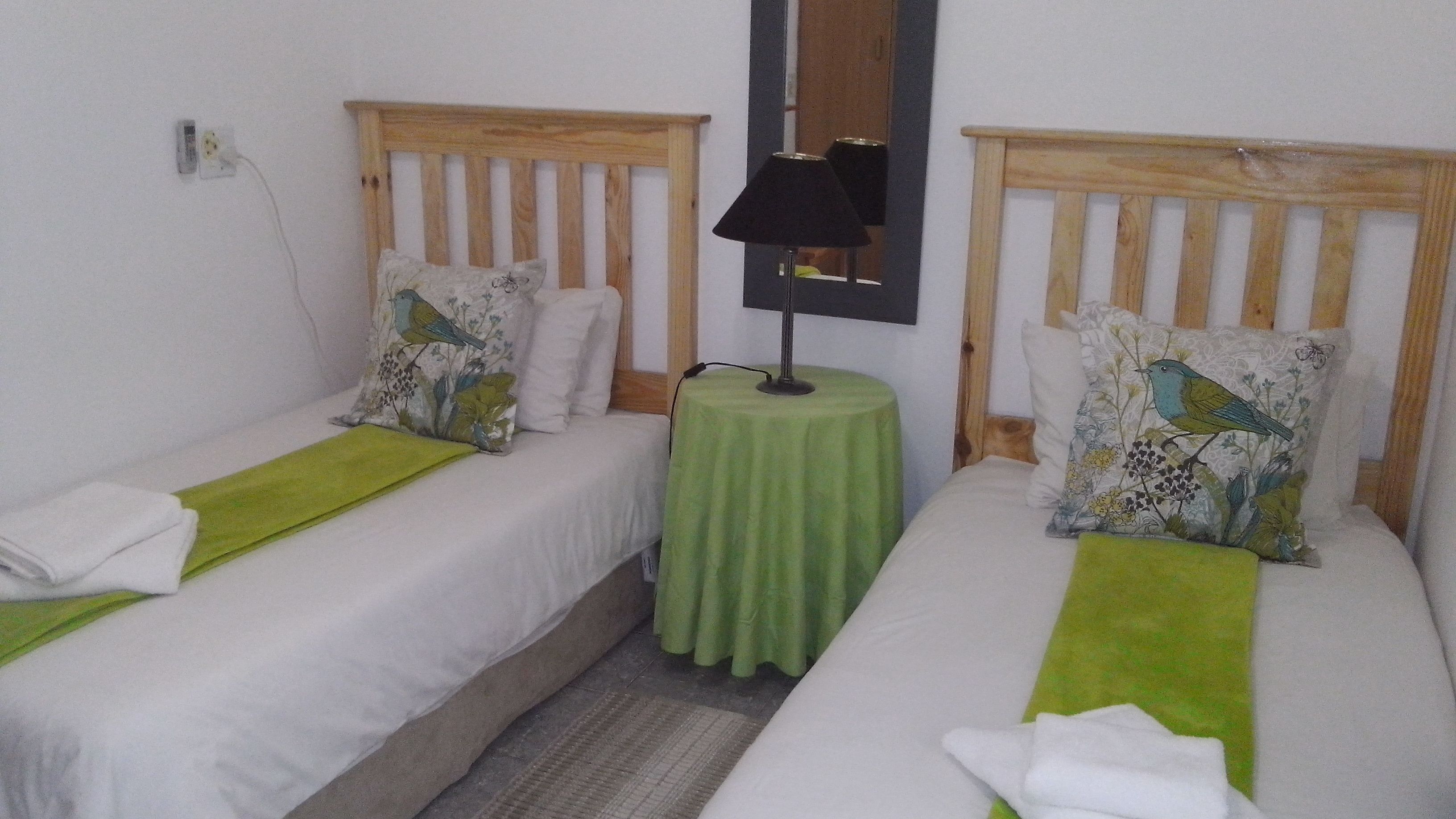 Habitación doble con dos camas individuales, cada una con cabecero de madera, una mesa verde y una lámpara.