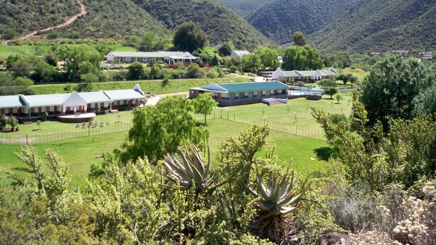 A rural hotel with multiple buildings, a fenced lawn, and a mountainous backdrop.