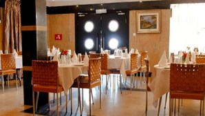 Un espace repas avec des tables et des chaises rondes, un mur noir orné de fenêtres circulaires et un tableau encadré accroché au mur.