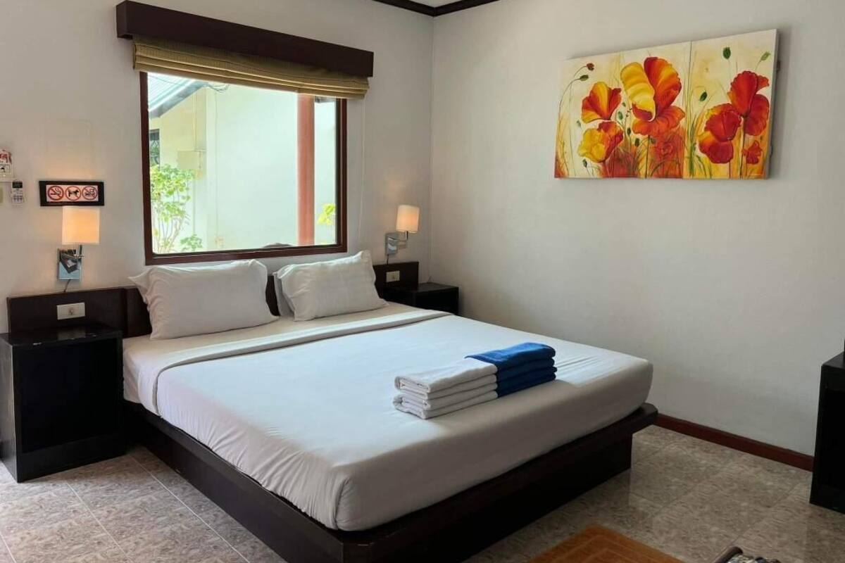 A hotel room with a bed, two bedside tables, a window with a blind, a painting on the wall, and a view of the outdoors.