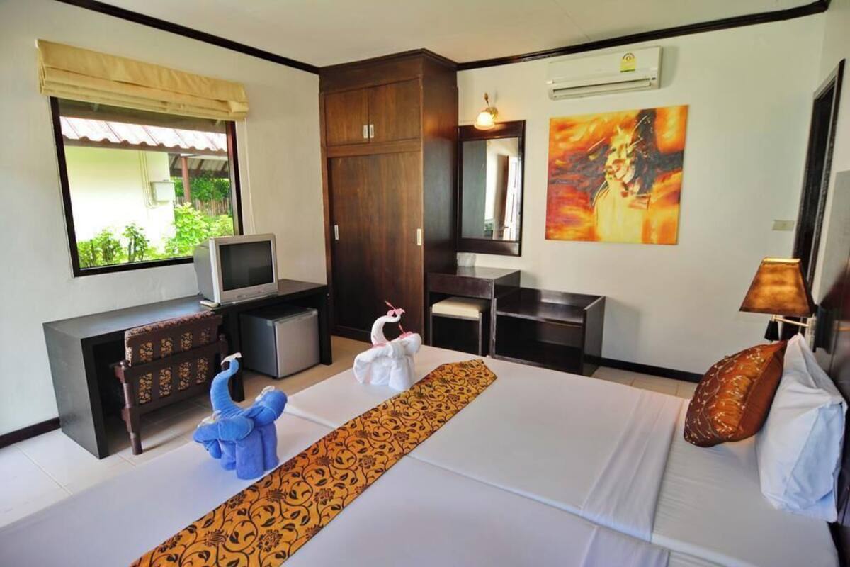 A hotel room with a bed, a television, a wardrobe, a desk, a chair, a window with a view, and a painting on the wall.