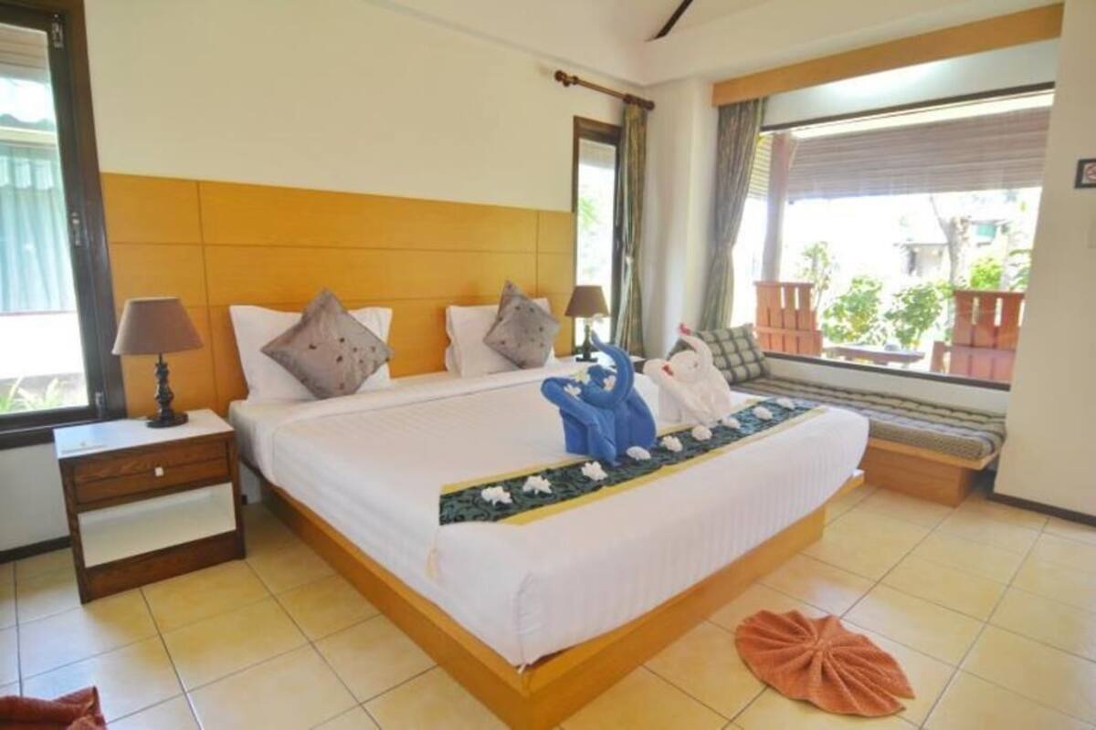 A hotel room with a bed, bedside tables, a window with a view, and a bench by the window.