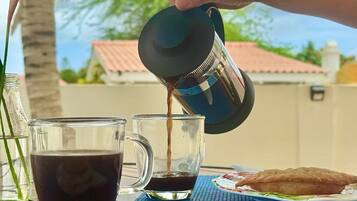 A hand pouring coffee into a glass mug, with a palm tree and a house in the background.