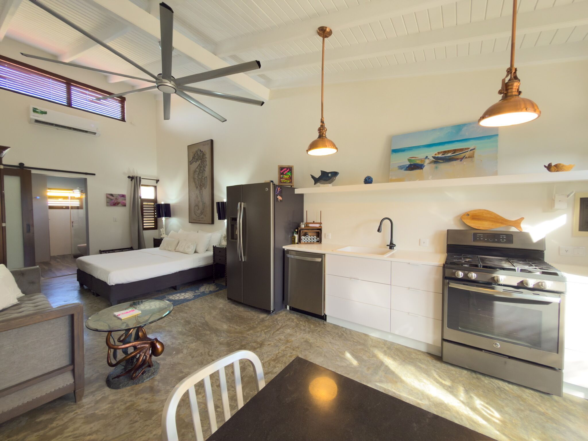 A compact living space with a bed, kitchenette, dining area, and a ceiling fan.