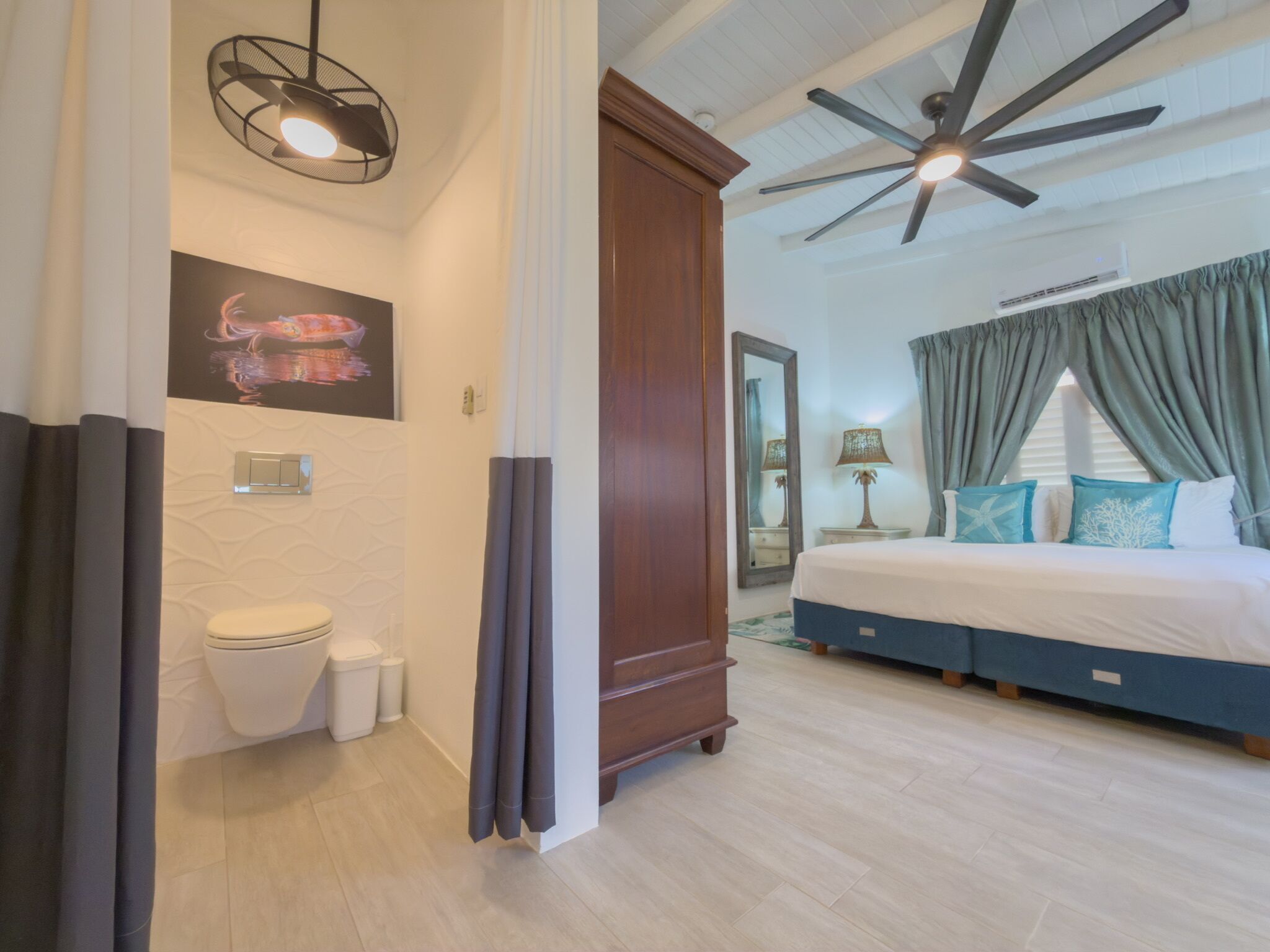 A bedroom with a bed, a ceiling fan, a nightstand, a lamp, and a bathroom with a toilet and a shower curtain.