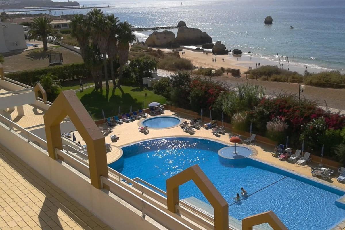 Una piscina de hotel con dos secciones, vistas a la playa y un litoral rocoso.
