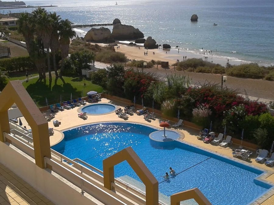 Una piscina de hotel con dos secciones, vistas a la playa y un litoral rocoso.