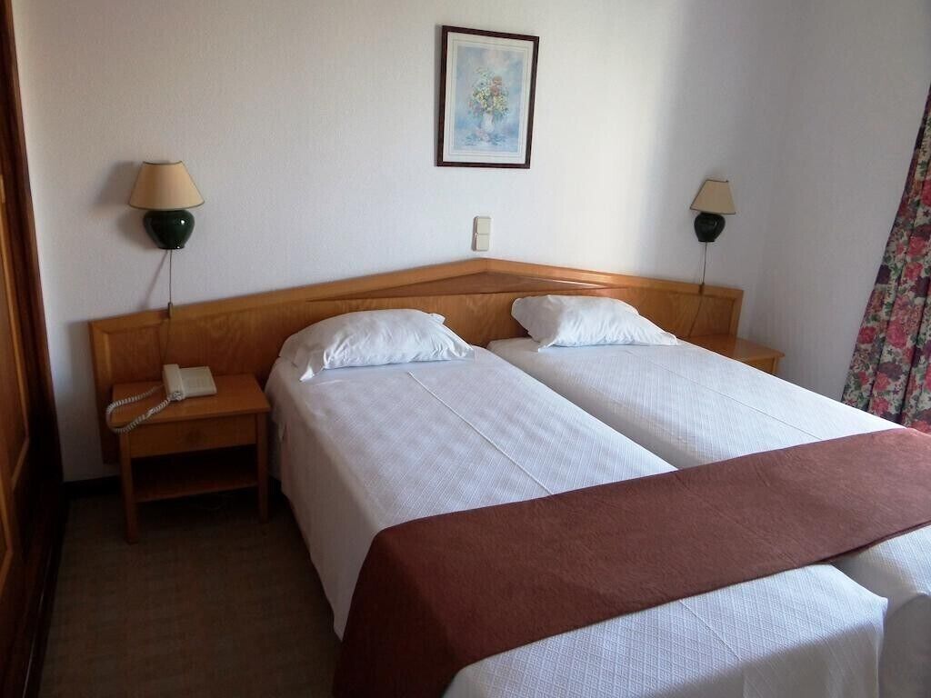 A hotel room with two beds, a wooden headboard, bedside lamps, a telephone, and a framed picture on the wall.
