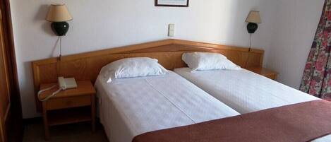 Habitación de hotel con dos camas, cabecero de madera, lámparas de noche, teléfono y un cuadro en la pared.
