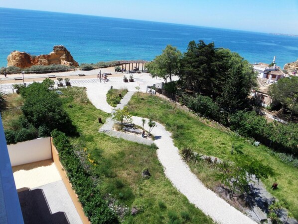 A coastal area with a paved walkway, greenery, and a view of the sea.