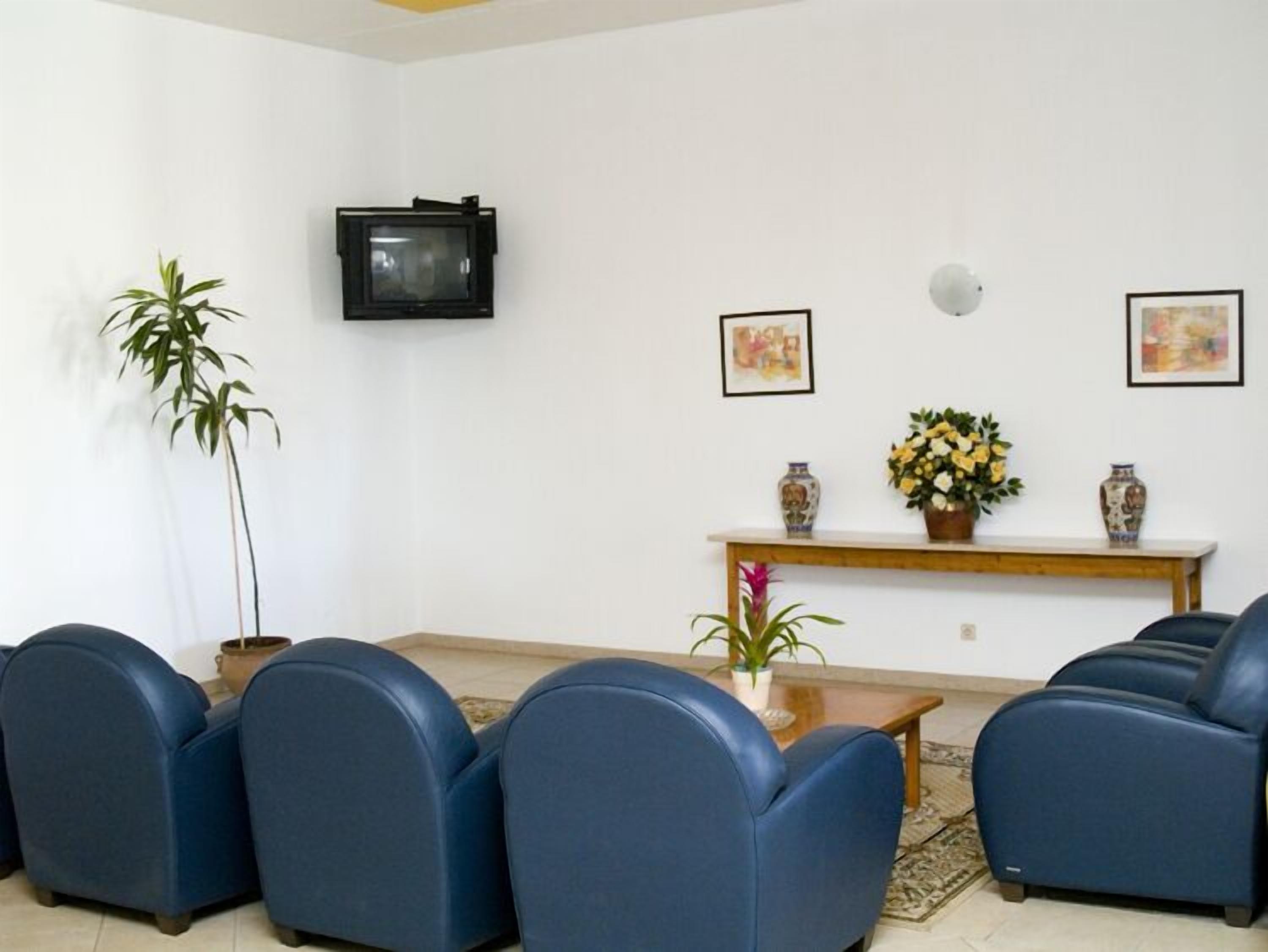 A waiting area with blue chairs, a small table, a wall-mounted TV, and two framed artworks.