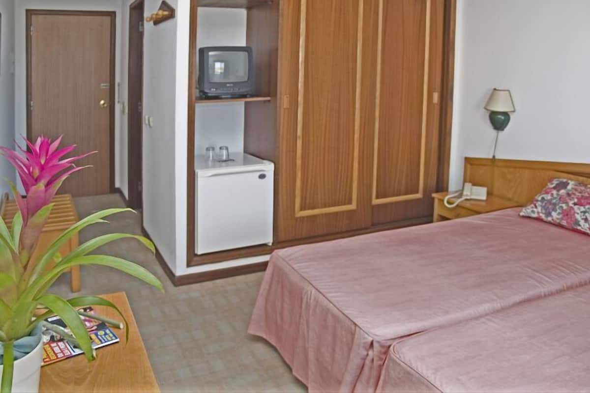 Un dormitorio con cama, mesita de noche, lámpara, televisor en un estante y armario.