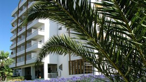 A multi-story hotel with balconies, a landscaped garden with purple flowers, and a palm tree in the foreground. - Hotel Luar (Portimão)