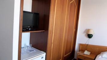 Habitación de hotel con un armario de madera, un televisor en una estantería, una mesita de noche con lámpara y una cama.