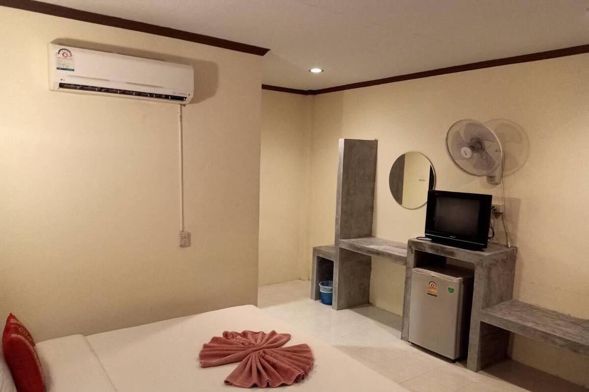 Una habitación de hotel con cama, escritorio, televisor, espejo y aire acondicionado.