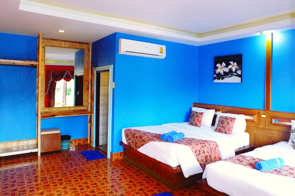 Una habitación de hotel con una cama grande, una mesita pequeña, un espejo y un equipo de aire acondicionado.