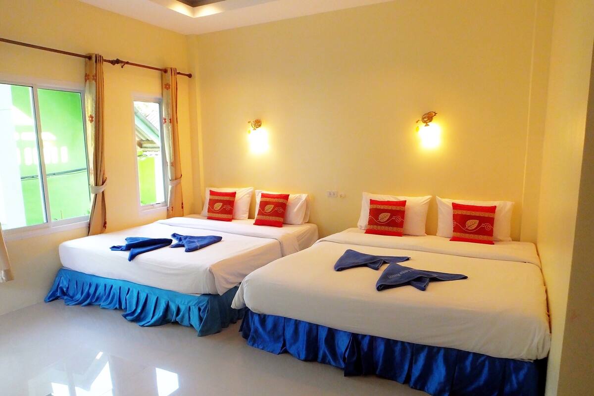Habitación de hotel con dos camas, cada una con cubrecama azul y almohadas decorativas rojas.