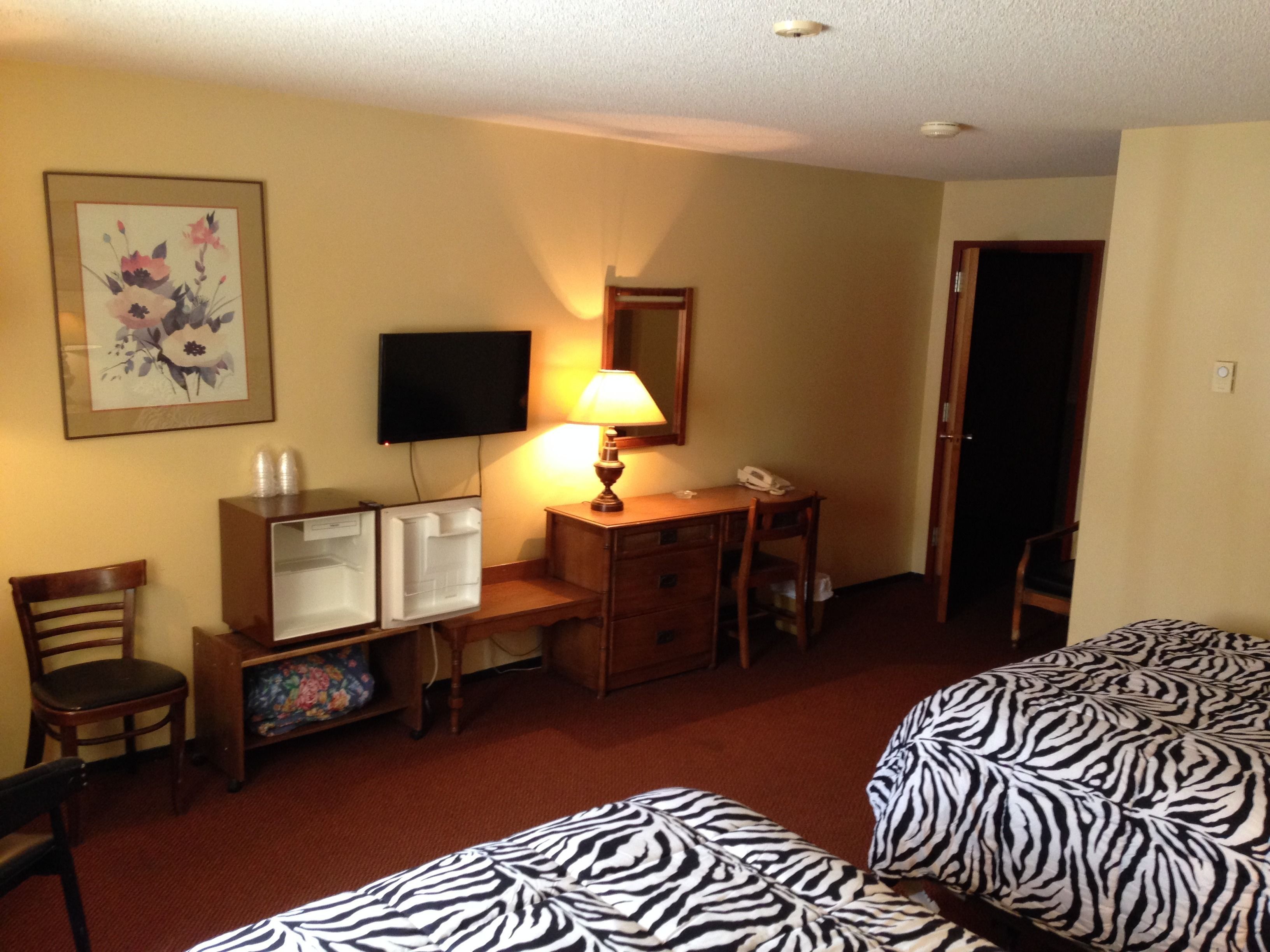 A hotel room with two beds, a desk with a lamp, a television, and a refrigerator.