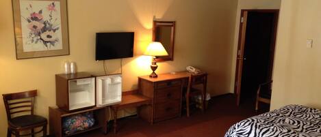 A hotel room with two beds, a desk with a lamp, a television, and a refrigerator.