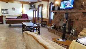 Un espacio lounge acogedor con mesa de billar, asientos cómodos, televisor y chimenea.