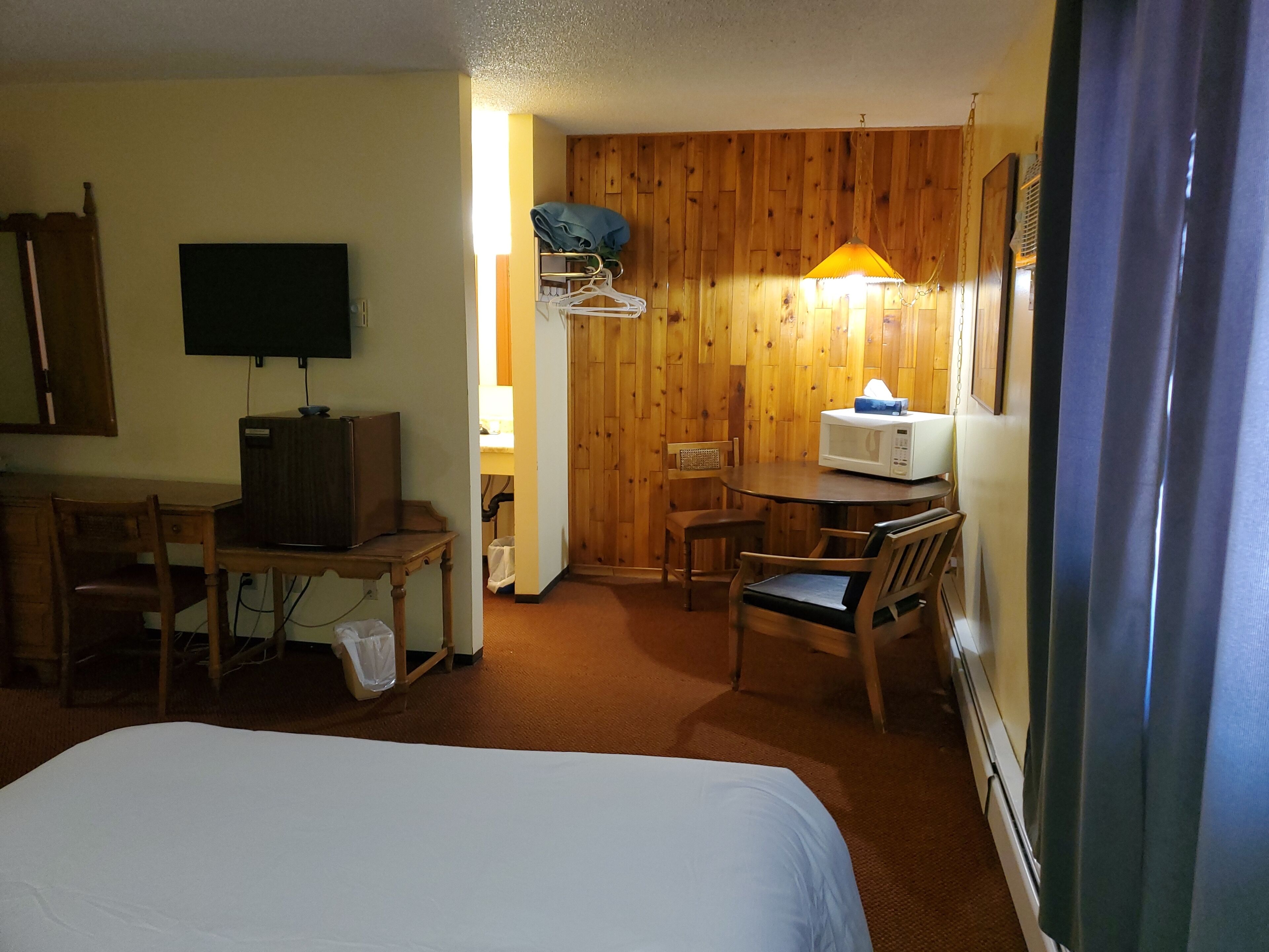 Habitación de hotel con una cama, un escritorio con computadora, un microondas y un televisor.