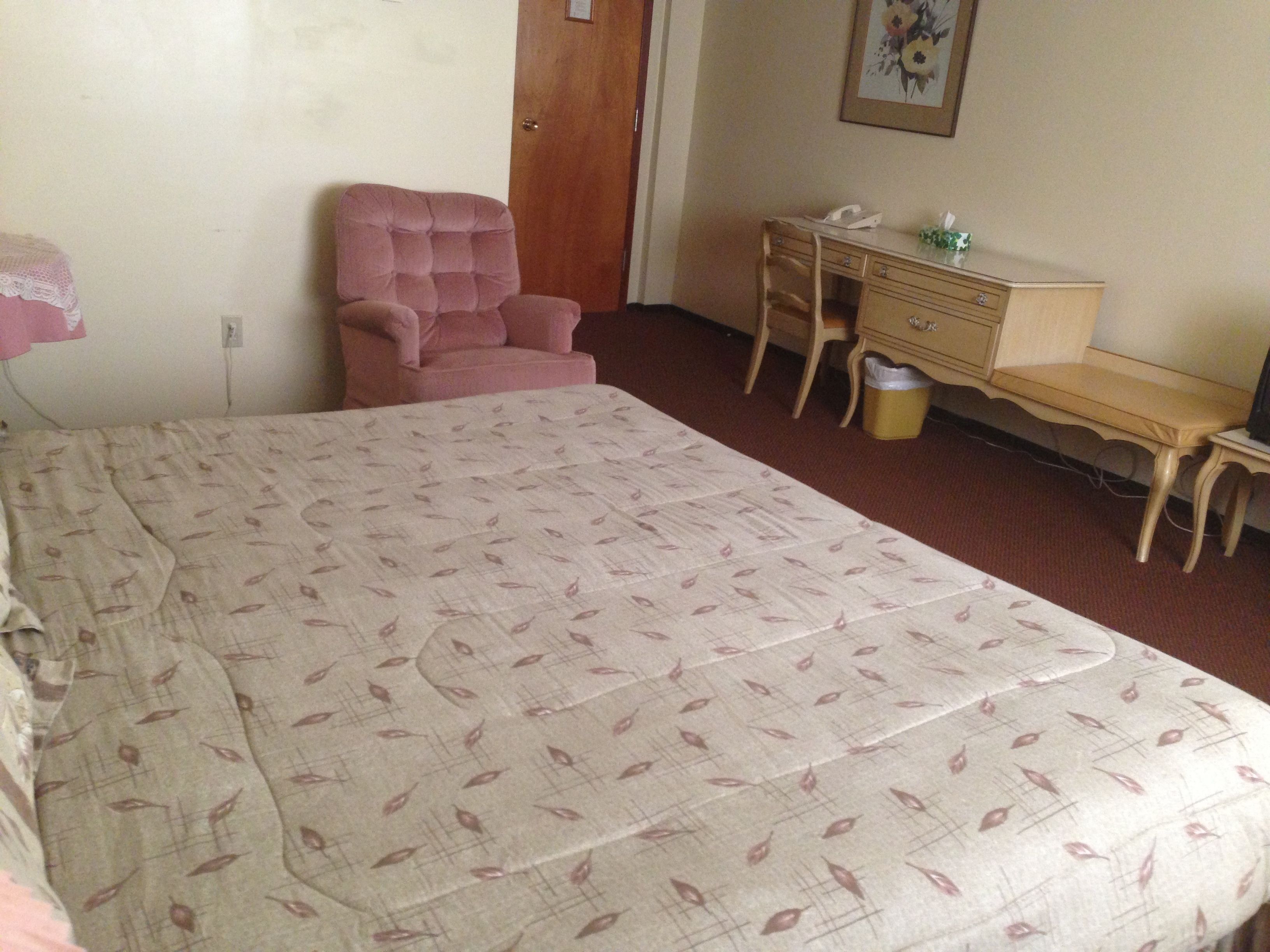 A bedroom with a bed, a pink armchair, a wooden desk, and a dresser.