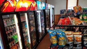 Una tienda de conveniencia con dispensadores de bebidas frías, bolsas de snacks y una gran variedad de productos envasados.