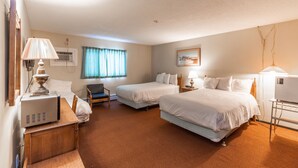 Habitación de hotel con dos camas, un escritorio con lámpara, una silla, un televisor y un cuadro en la pared.