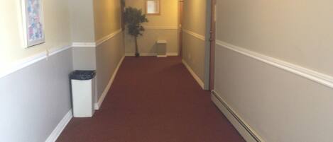 A hallway with a red carpet, white trim, and a trash can on the left.
