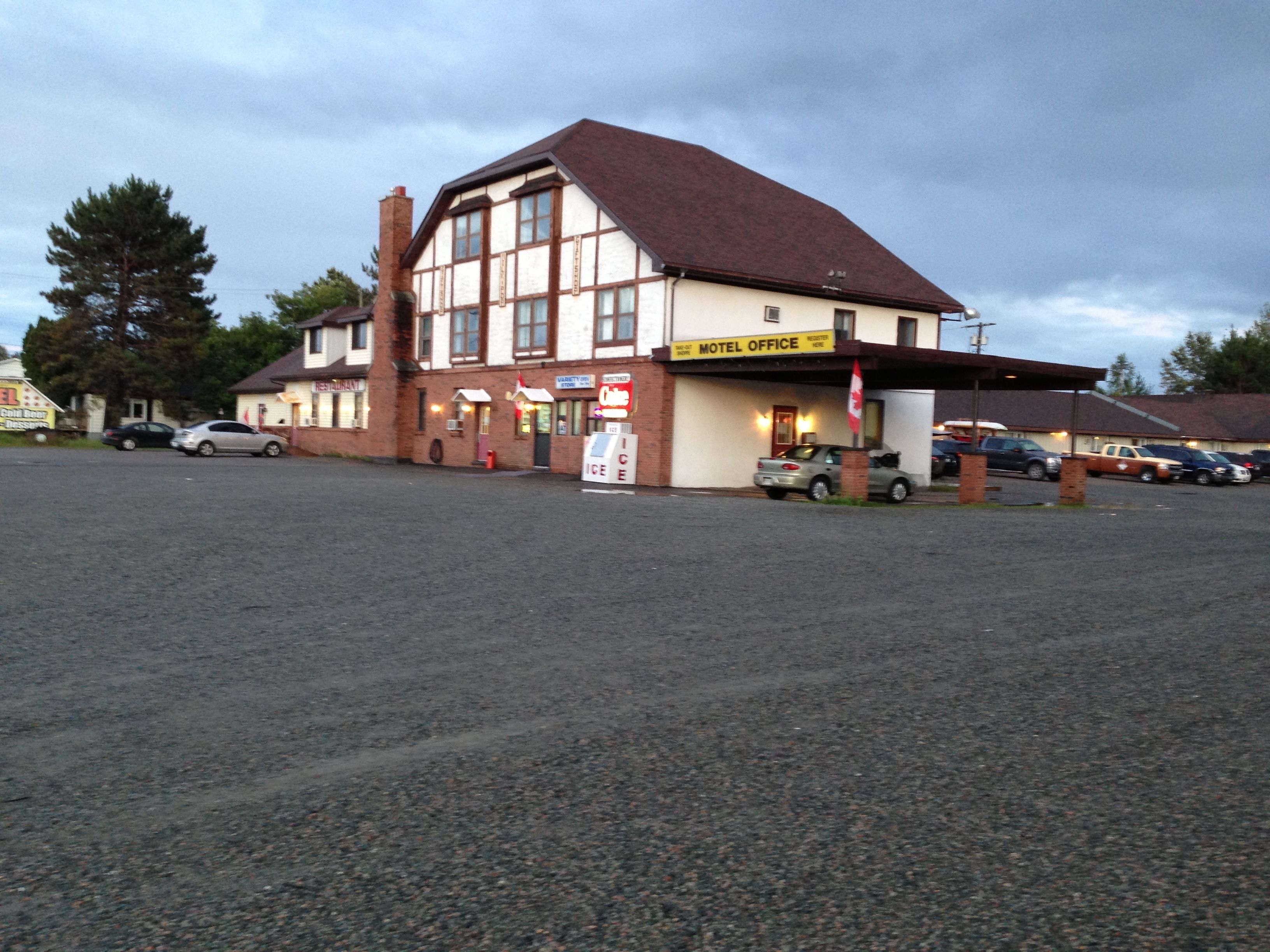 Een motel receptie met een bord, een parkeerplaats en een gebouw met een rood dak.