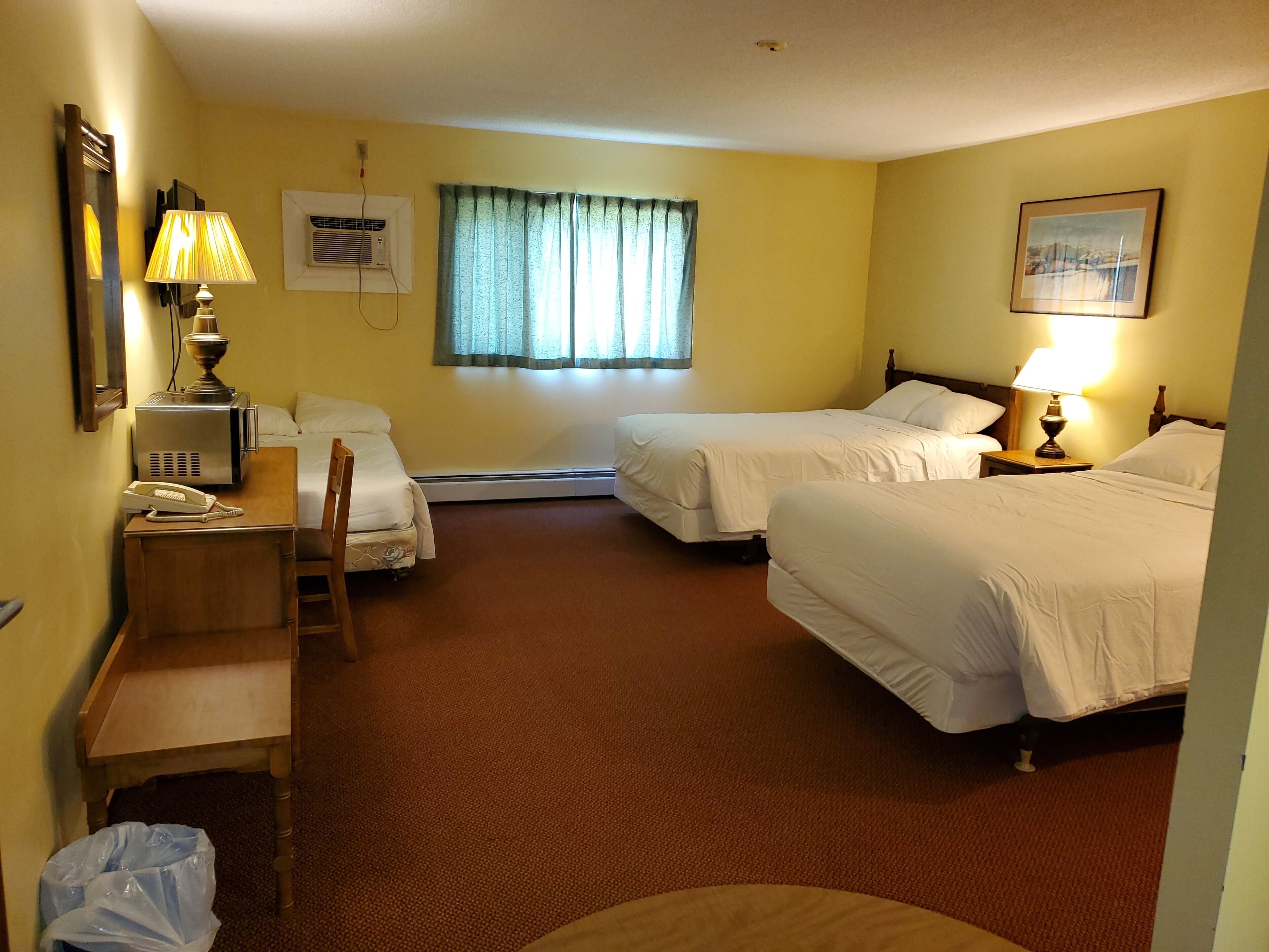 A hotel room with two beds, a desk with a lamp, a telephone, and a window with curtains.
