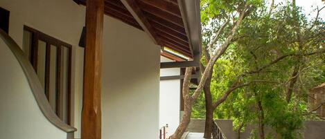 A wooden covered walkway with a railing, leading to a building with a white exterior.