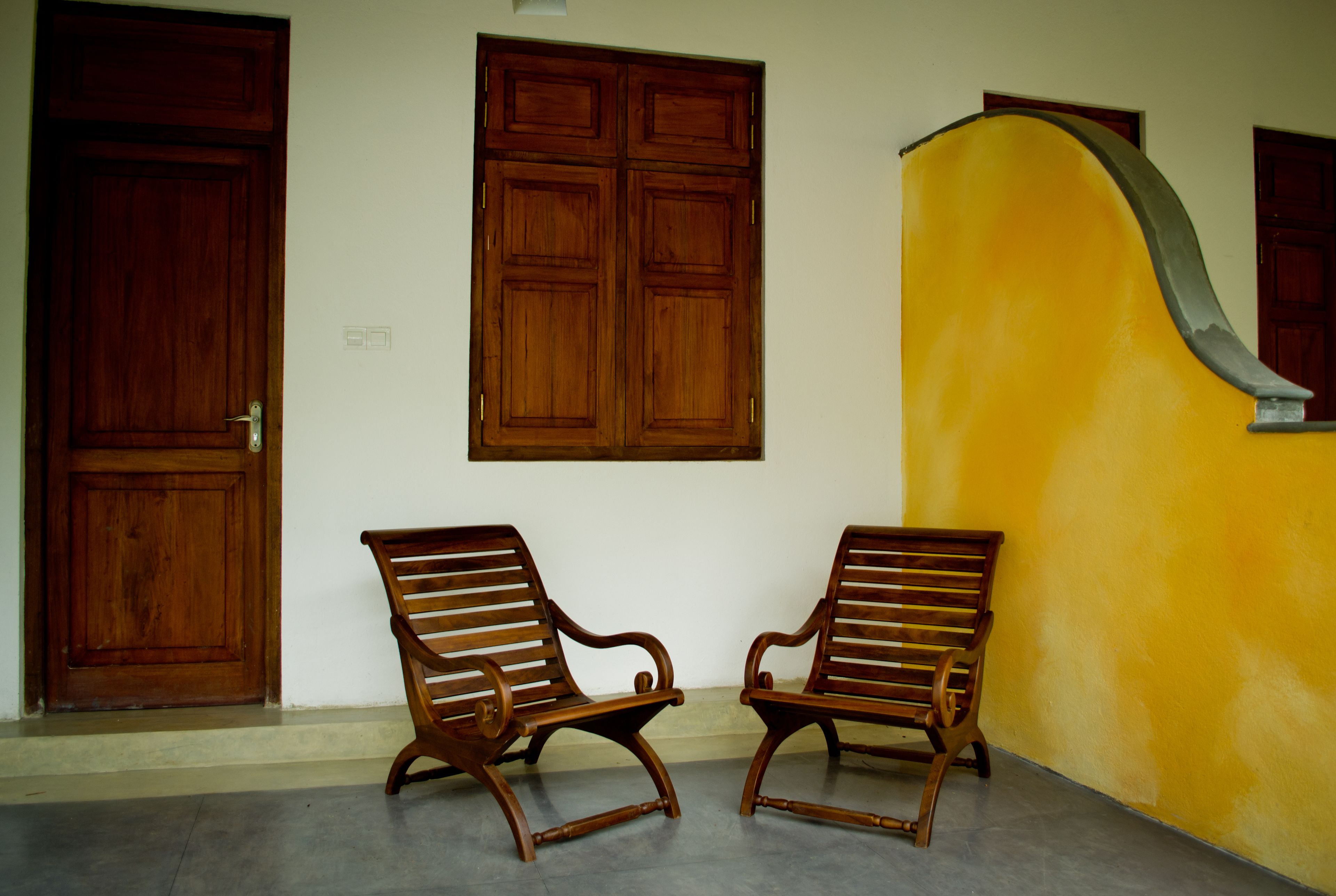 Two wooden chairs against a wall with a wooden door and window.