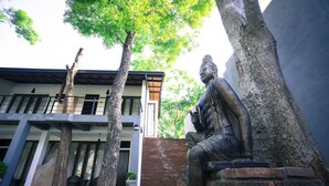 A statue of a seated figure in a courtyard with a modern building in the background. - Hotel Alakamanda (Anuradhapura)