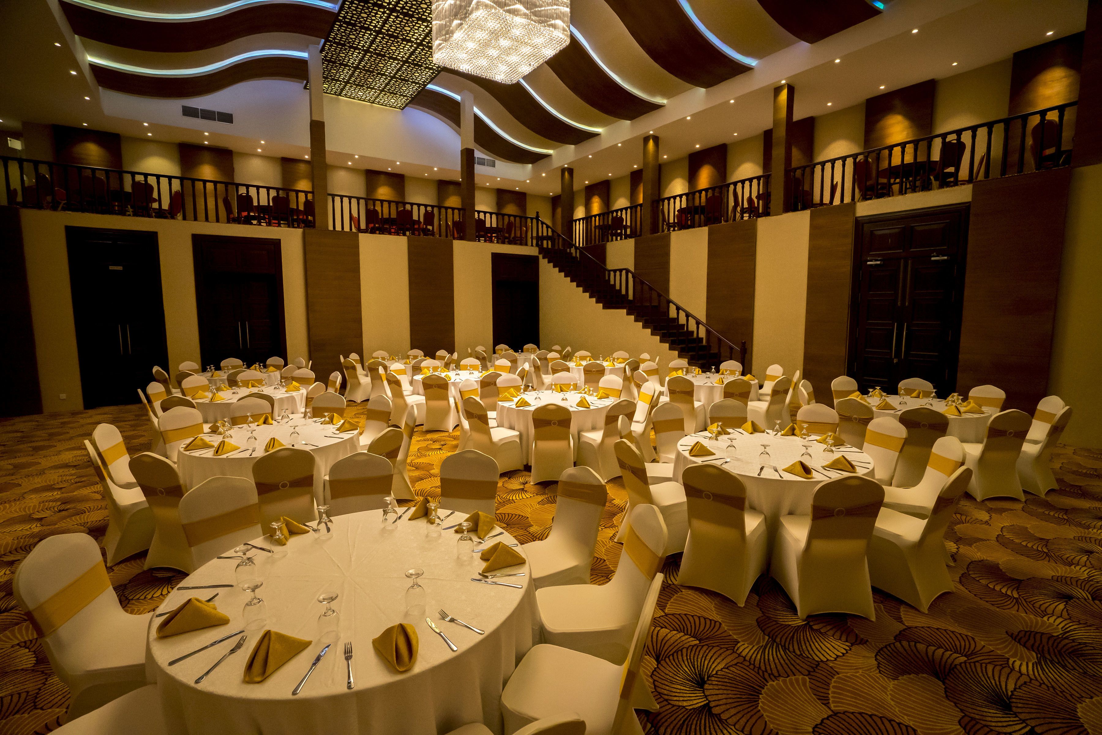A banquet hall with round tables, white chairs, and a staircase.