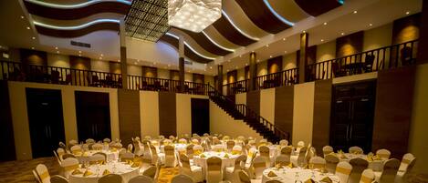 A banquet hall with round tables, white chairs, and a staircase.