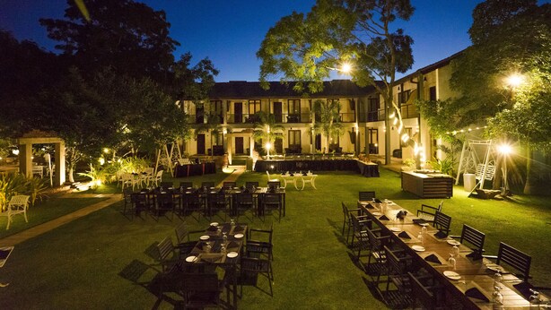 An outdoor dining area with tables and chairs, surrounded by a well-maintained lawn and trees. - Hotel Alakamanda (Anuradhapura)